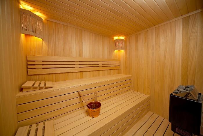 Modern ahşap panelli bir sauna odasının içi, otantik sauna taşları ve sıcak ortam aydınlatması.